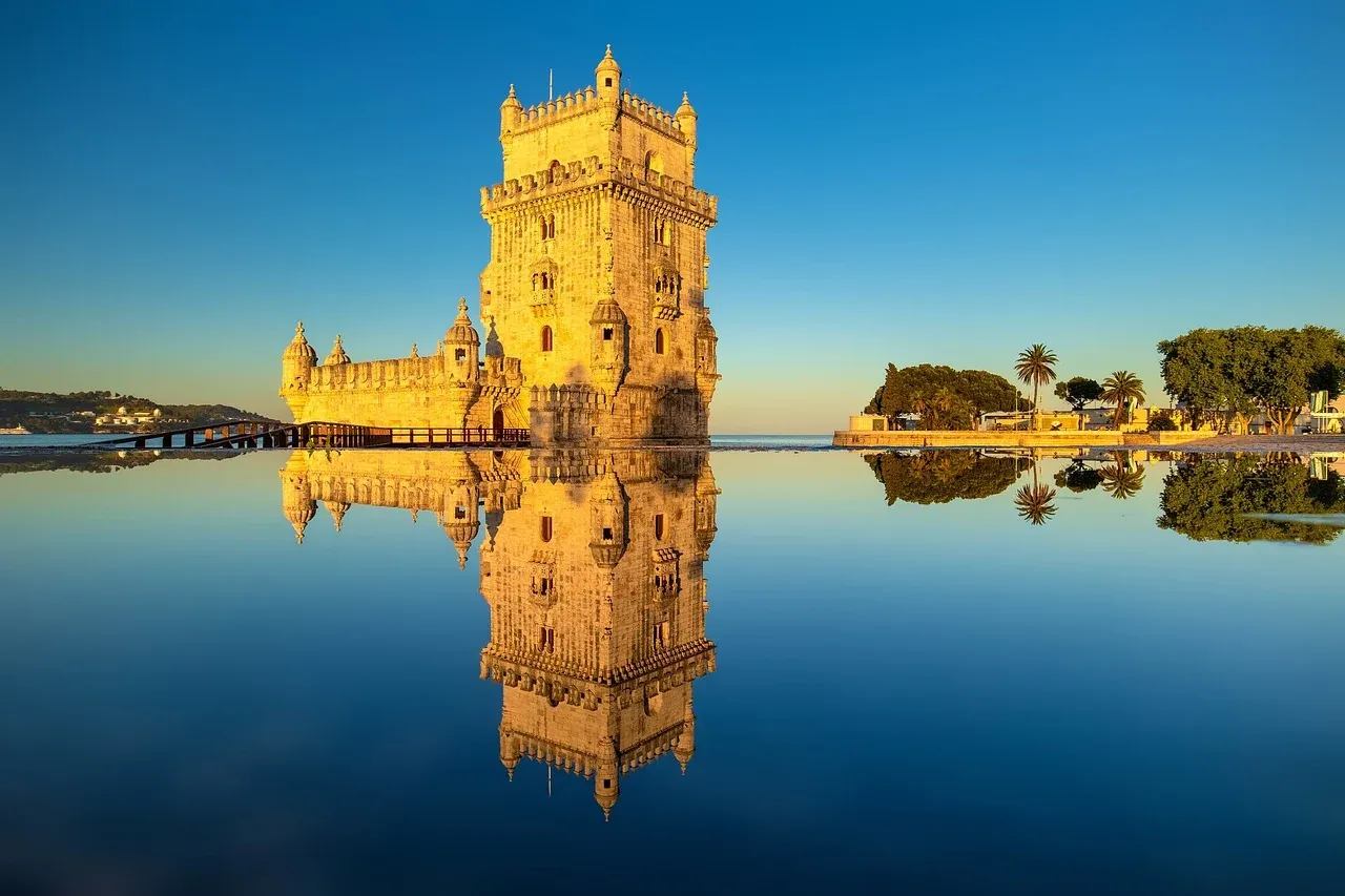 Torre de Belém iluminada pelo sol ao fim do dia, refletida perfeitamente na água